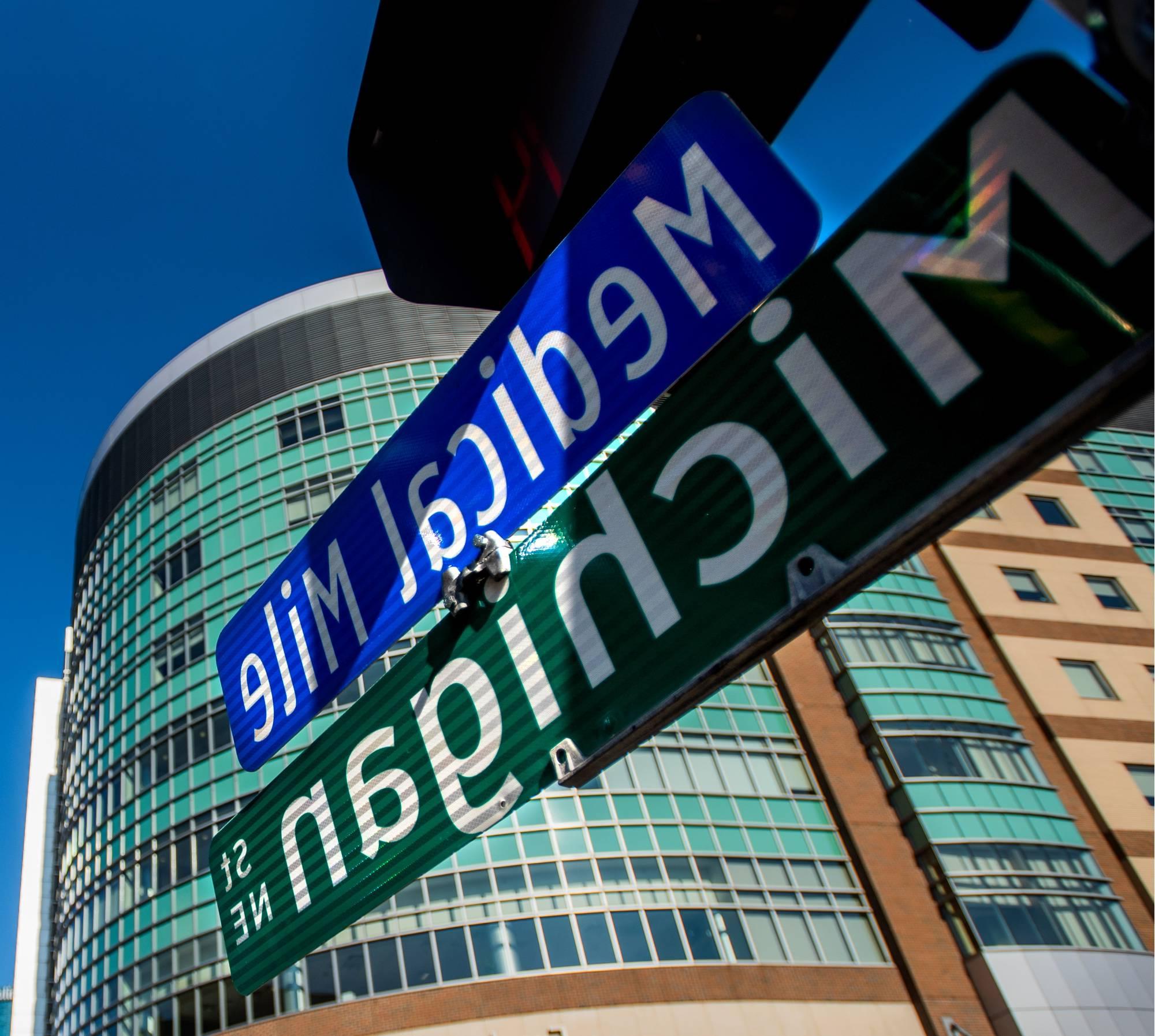 Close up photo street signs listing "Michigan Street NE" and "Medical Mile", with a medical building in the distance.